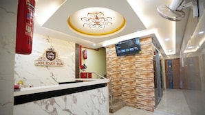 A hotel reception area with a marble counter, a digital screen, and a stone wall. - RMA Joliday Inn (Pondicherry)