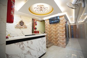 Een hotel receptie met een marmeren balie, een digitaal scherm en een stenen muur.