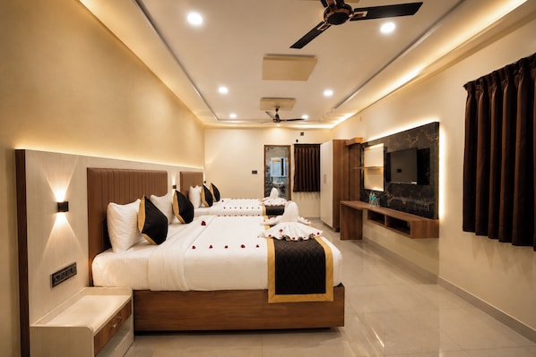 A modern hotel room with a large bed, bedside tables, a ceiling fan, and a flat-screen TV mounted on the wall.