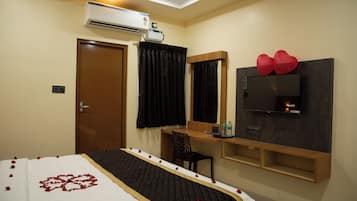 Een hotelkamer met een bed, een bureau met stoel, een flatscreen televisie, een airconditioner en een deur.