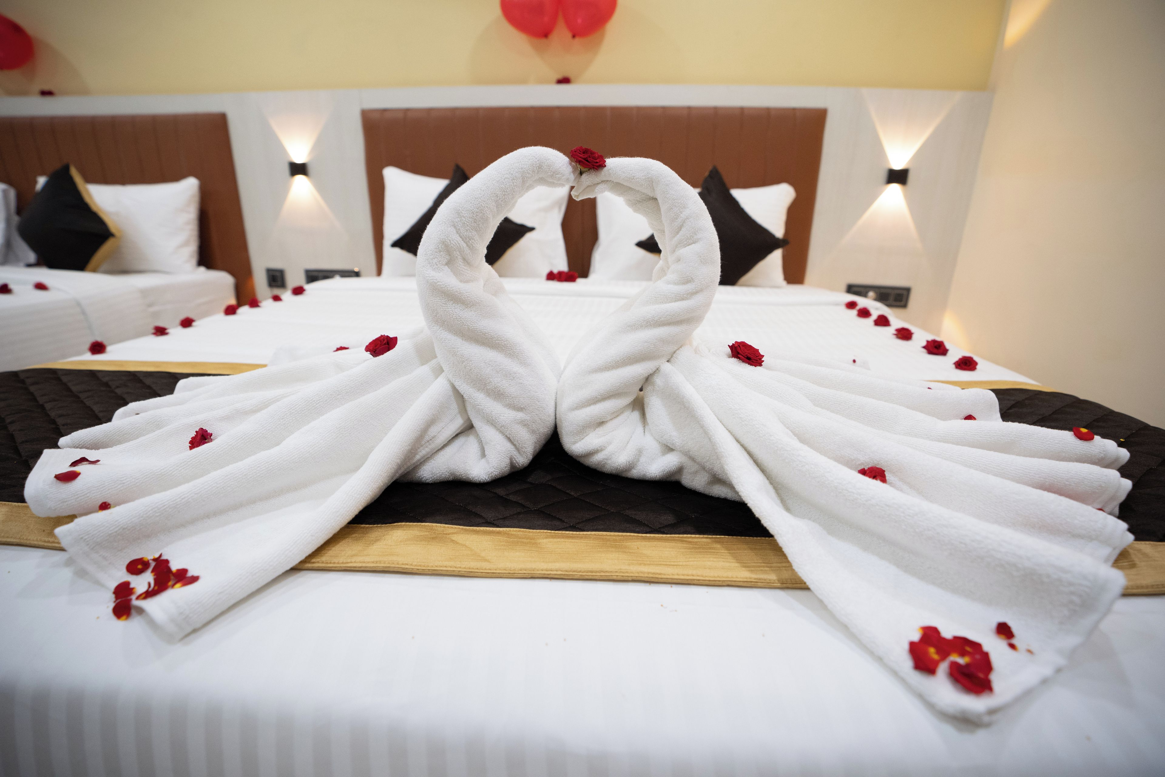 A bed with a towel arrangement in the shape of two swans, with rose petals scattered around.