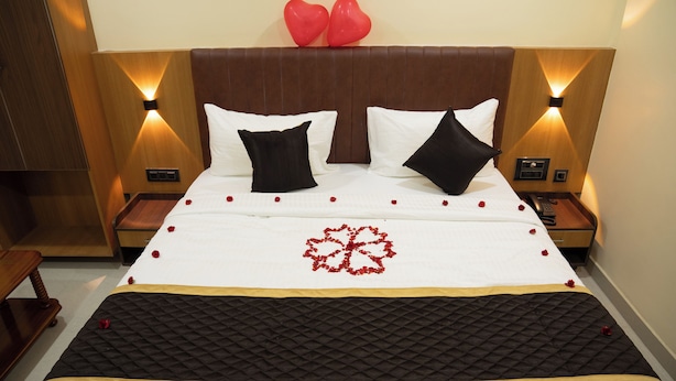 A hotel room with a bed, two bedside tables, a wooden headboard, and a wall-mounted light fixture. - RMA Joliday Inn (Pondicherry)