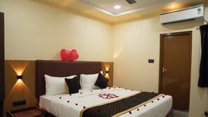 A hotel room with a bed, bedside tables, a wardrobe, and an air conditioning unit. - RMA Joliday Inn (Pondicherry)