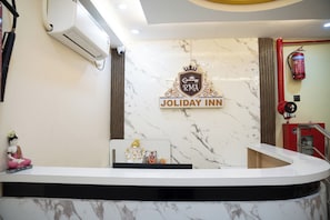 A reception desk with a marble wall, a sign for 'JOLIDAY INN,' and a fire extinguisher. - RMA Joliday Inn (Puducherry)