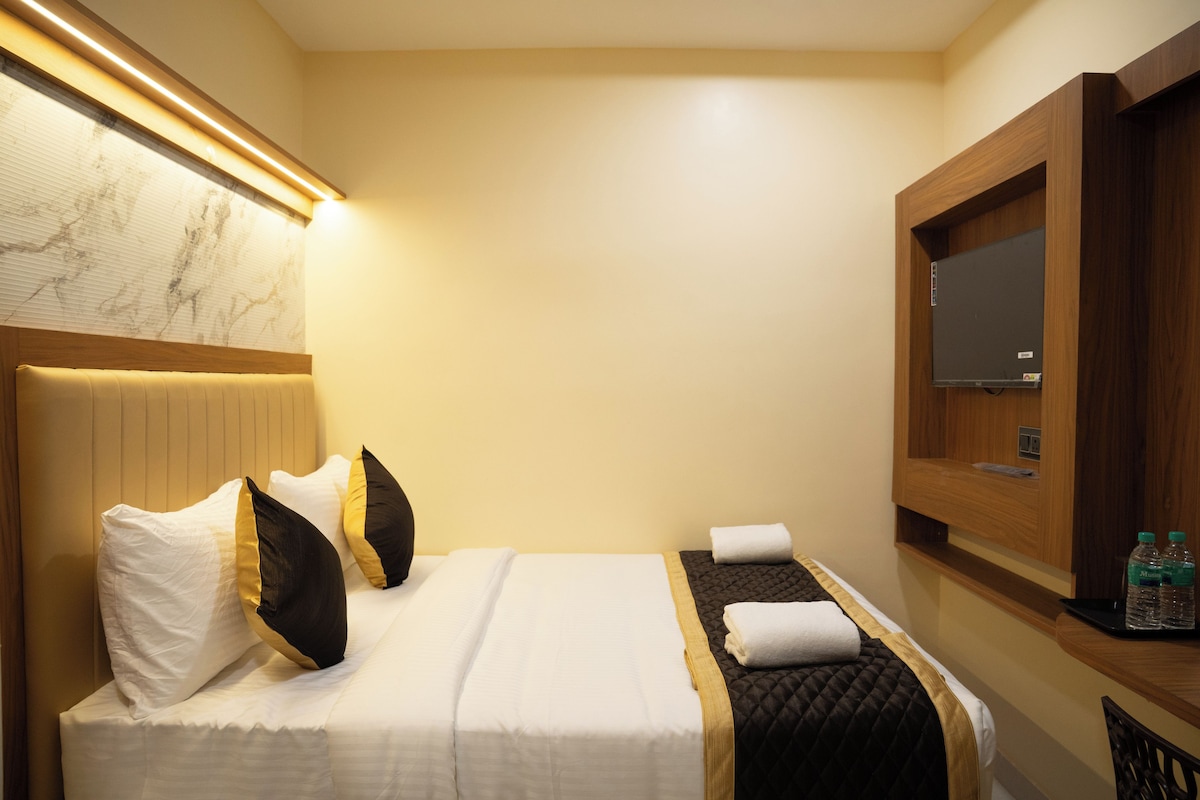 A hotel room with a bed, a headboard, a bedside table, a mirror, and a wall-mounted TV.