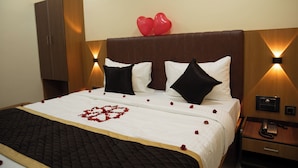 A hotel room with a bed, a wooden wardrobe, a bedside table with a phone, and a wall-mounted light fixture. - RMA Joliday Inn (Pondicherry)