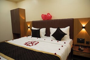 Een hotelkamer met een bed, een houten kledingkast, een nachtkastje met telefoon en een wandlamp.