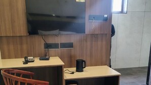 Et hotelværelse med seng, skrivebord med stol, fjernsyn og kaffemaskine.