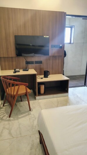 Habitación de hotel con cama, escritorio con silla, televisor y cafetera.