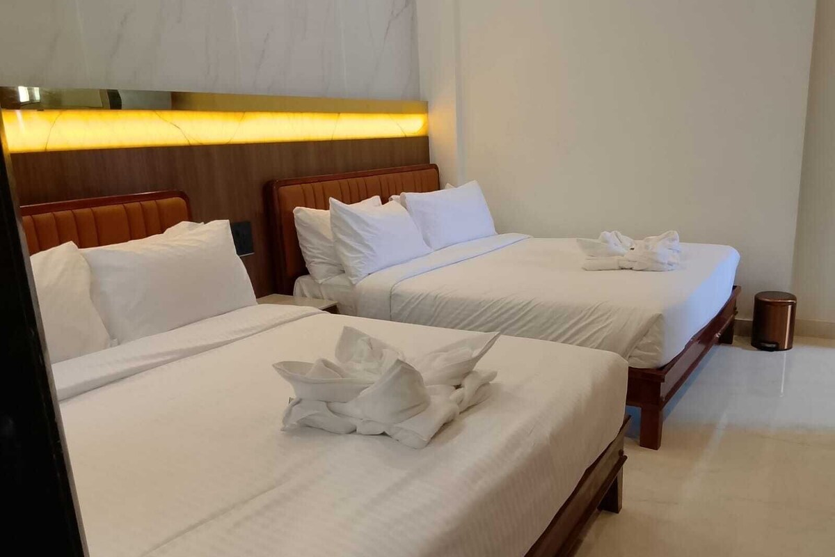 Habitación de hotel con dos camas, cada una con ropa blanca de cama y almohadas bien ordenadas.