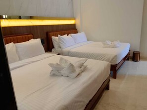 Habitación de hotel con dos camas, cada una con ropa blanca de cama y almohadas bien ordenadas.