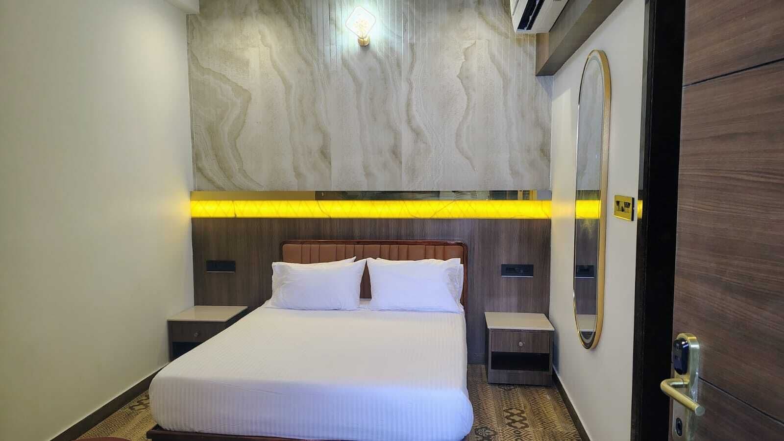 Una habitación de hotel con cama, mesitas de noche, un espejo y una puerta.