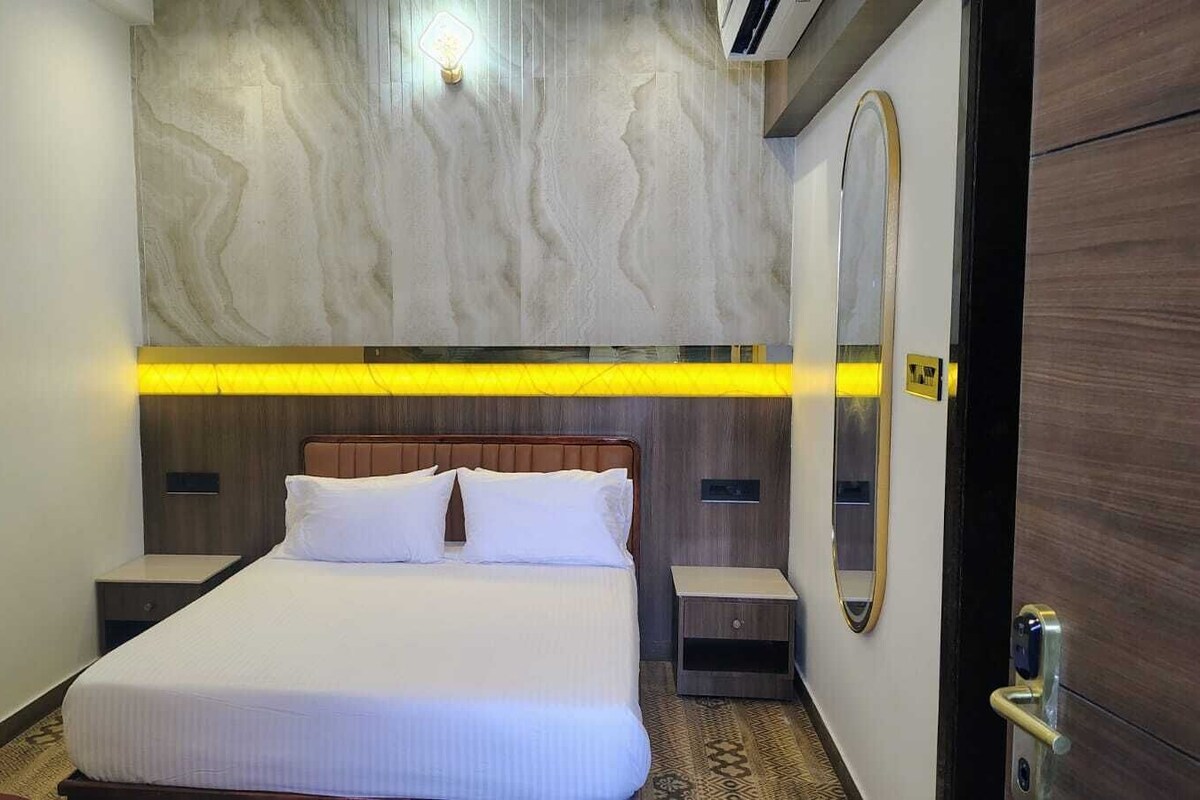 Una habitación de hotel con cama, mesitas de noche, un espejo y una puerta.