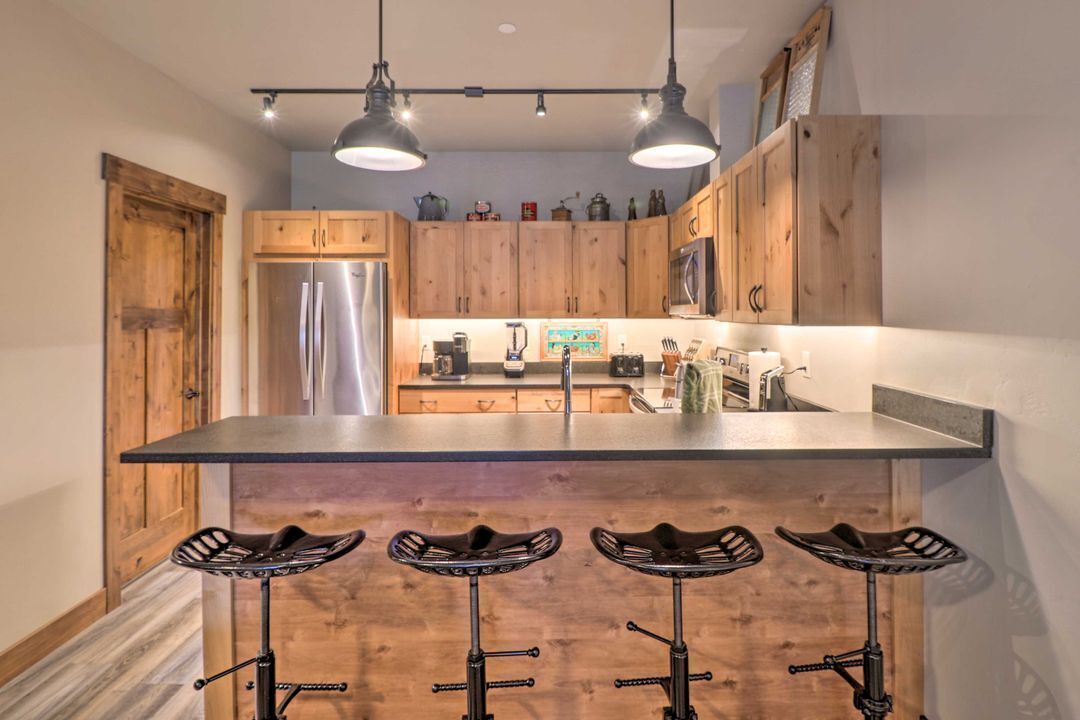 A kitchen with wooden cabinets, a stainless steel refrigerator, a bar stool area, and pendant lighting.