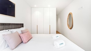 Un dormitori modern amb llit, almoinos, un armari, un mirall i una tovallola amb la marca 'HOMEBASE'.