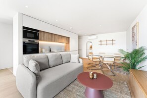 A modern living space with a sofa, a dining table with chairs, a kitchen area with appliances, and a large mirror. - Modern Family Apartment in Canidelo, Porto (Canidelo)
