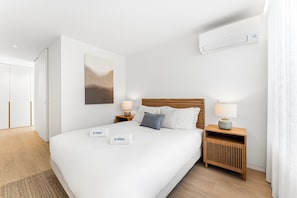 A hotel room with a large bed, two bedside tables with lamps, a wall-mounted air conditioner, and a painting on the wall. - Modern family apartment in Canidelo, Porto (Canidelo)