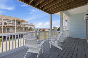A wooden deck with two Adirondack chairs, overlooking a residential area with a view of the ocean. - Emerality | Steps to Beach, Private Elevator (Emerald Isle)