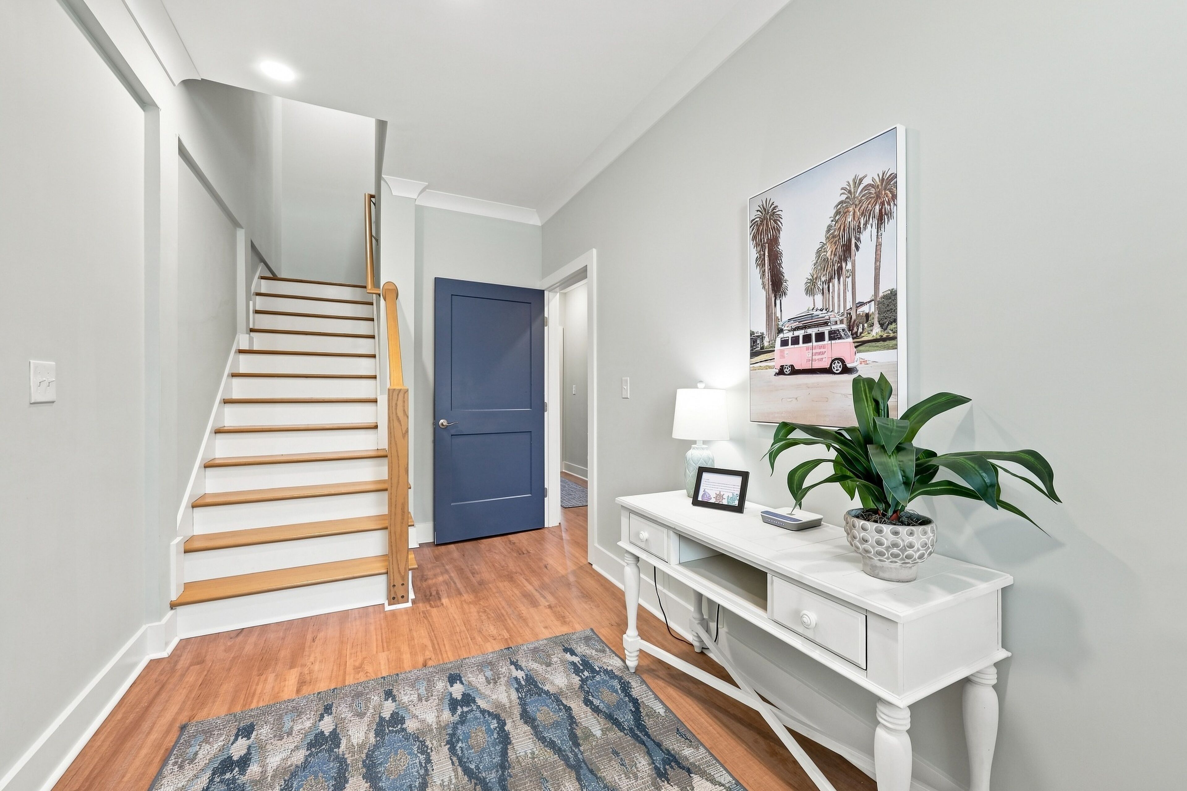A staircase leading to a door, a console table with a lamp and a framed picture, and a patterned rug.