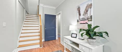 A staircase leading to a door, a console table with a lamp and a framed picture, and a patterned rug.