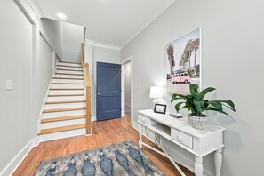 Un escalier menant à une porte, une console sur laquelle sont posés une lampe et un tableau encadré, et un tapis à motifs.