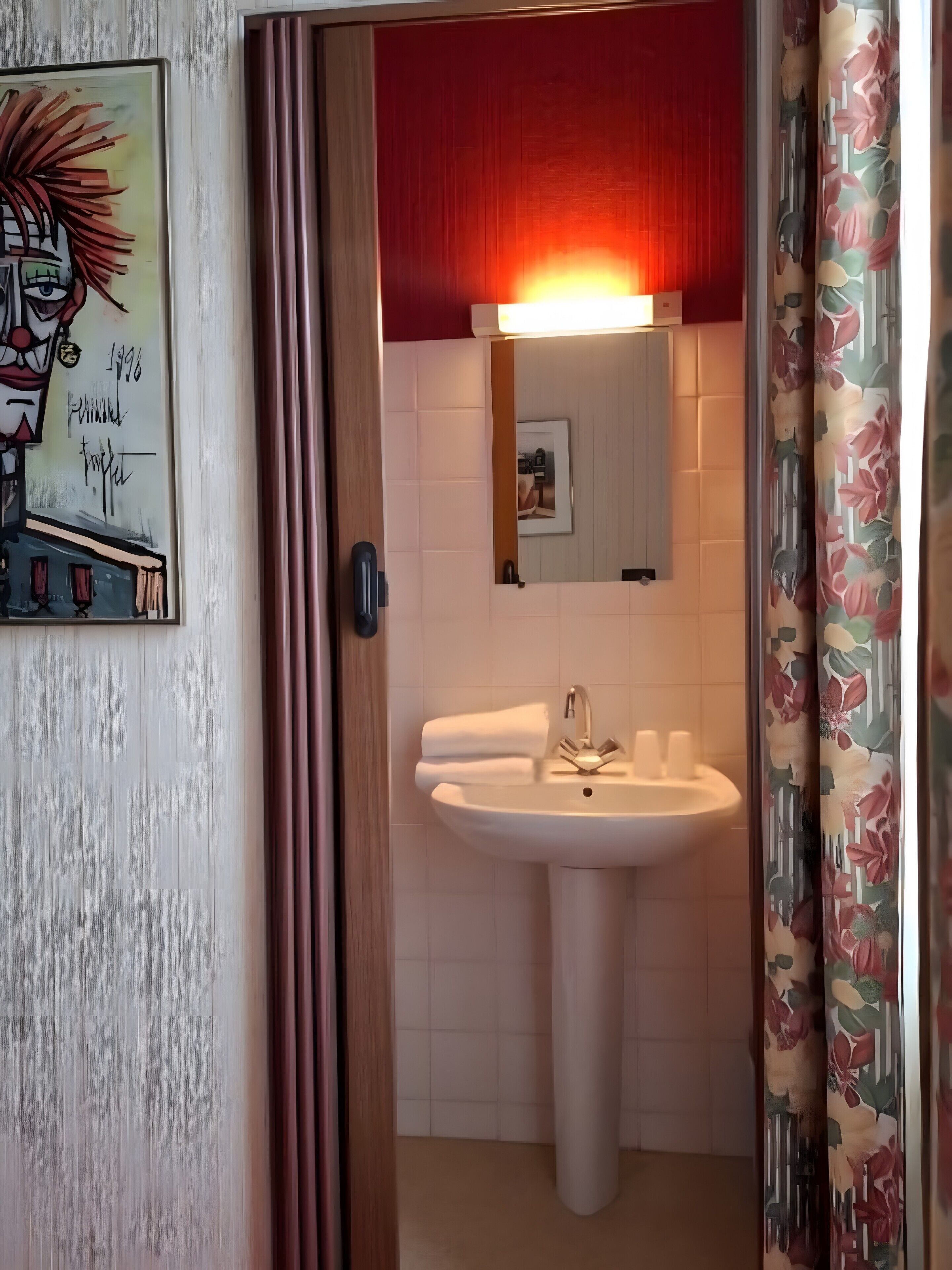 Een badkamer met een wastafel, spiegel en een deur naar een andere kamer.
