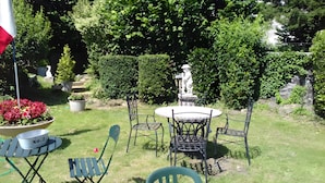 An outdoor seating area with a table and chairs, surrounded by greenery and a statue.