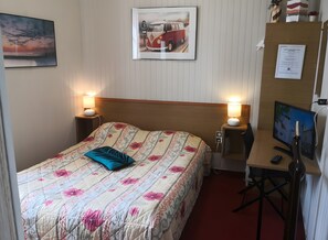 Ett hotellrum med en säng, sänglampor, ett skrivbord med en dator och en tv.