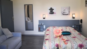 A bedroom with a bed, a sofa, a mirror, and wall-mounted lights.