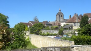 A historic building with a prominent tower, surrounded by lush greenery and a stone wall.