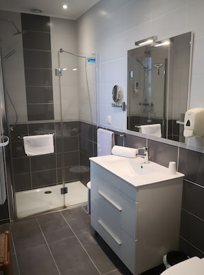 A modern bathroom with a glass-enclosed shower, a white sink, and a large mirror.