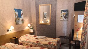 A hotel room with two beds, a desk, a chair, a mirror, wall-mounted lamps, and artwork.