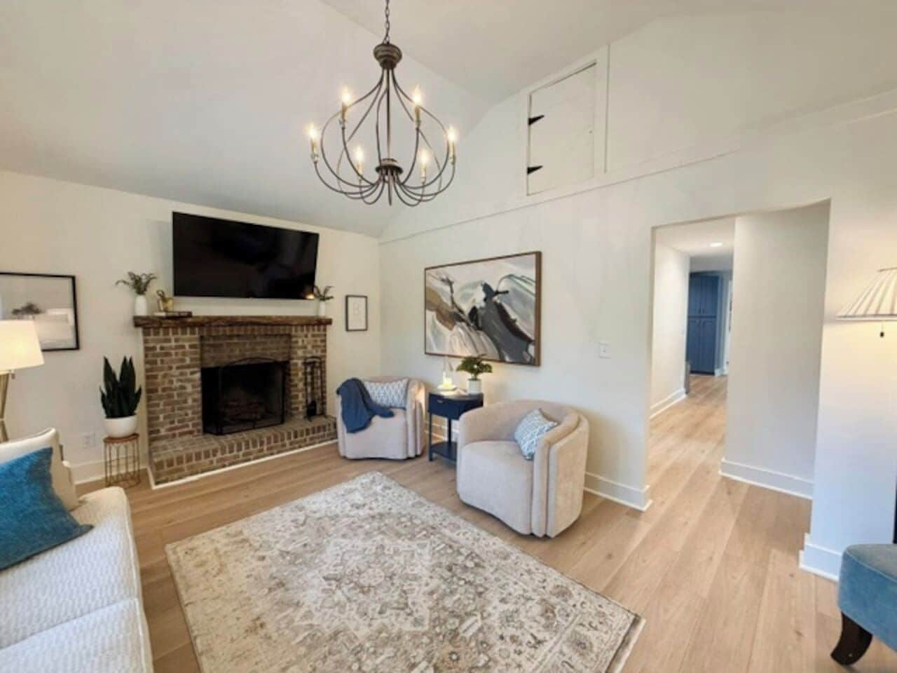 Una sala de estar con chimenea, televisor de pantalla plana, candelabro y alfombra grande.