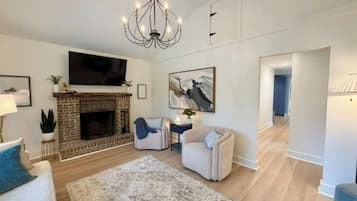 A living room with a fireplace, a flat-screen TV, a chandelier, and a large rug.
