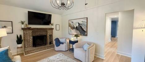 Una sala de estar con chimenea, televisor de pantalla plana, candelabro y alfombra grande.