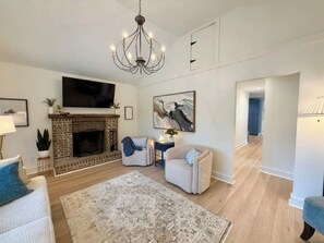 Uma sala de estar com lareira, TV de tela plana, lustre e um tapete grande.