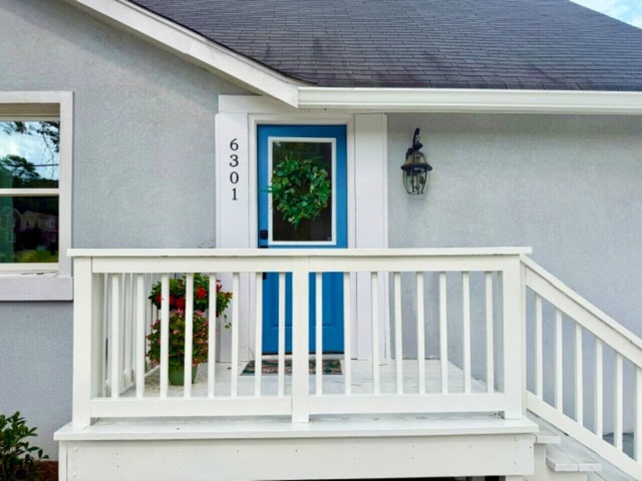 Une maison avec un porche blanc, une porte bleue et le numéro « 6301 » peint sur le mur.