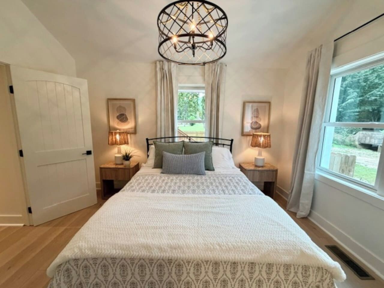 Une chambre à coucher avec un grand lit, deux tables de chevet avec des lampes, un luminaire au plafond et une fenêtre avec des rideaux.