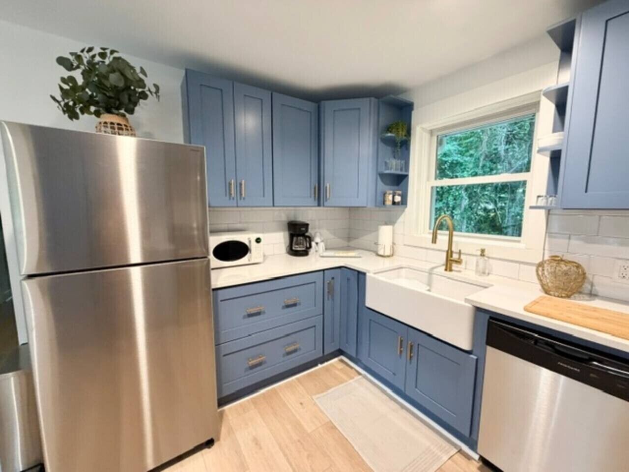Een moderne keuken met roestvrijstalen apparatuur, blauwe keukenkastjes en een raam met uitzicht op groen.