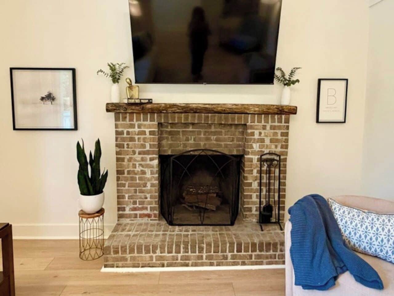 A living room with a brick fireplace, a television mounted above it, and a couch with a blanket.