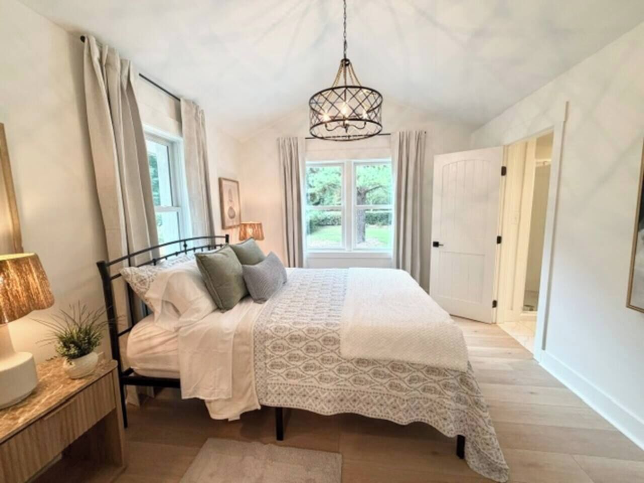 Een slaapkamer met een bed, nachtkastje, lamp en uitzicht op het groen.