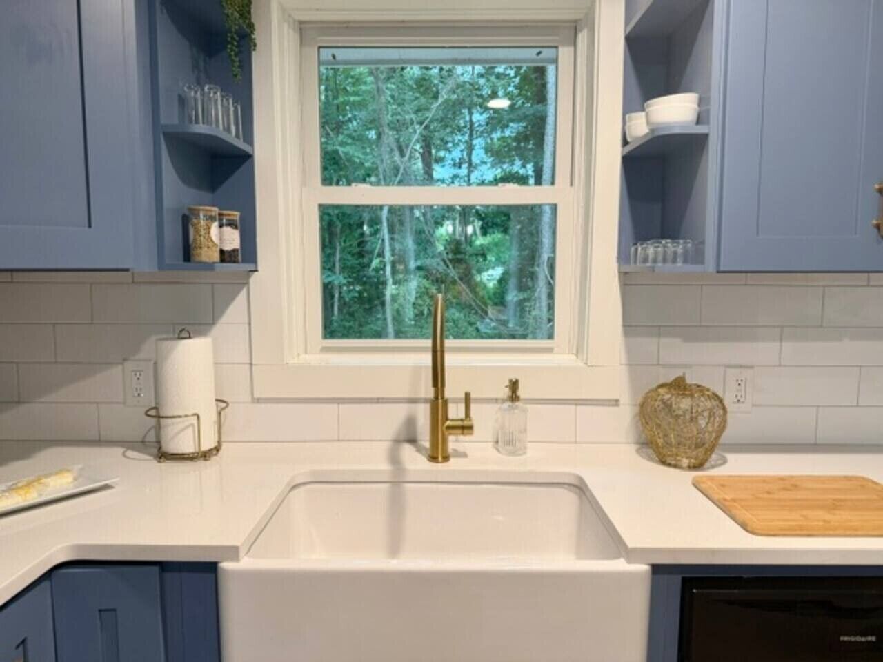 Eine Küche mit einem weißen Spülbecken, einem goldenen Wasserhahn und einem Fenster mit Blick auf Bäume.