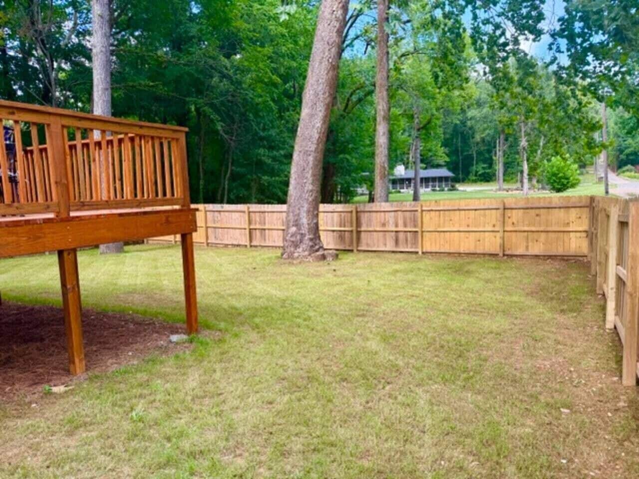 A wooden deck with a metal railing, surrounded by a wooden fence and trees.
