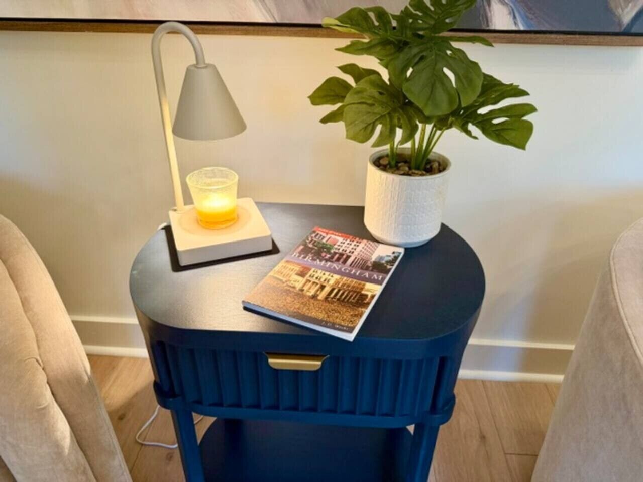 Een kleine ronde tafel met een lamp, een kaars, een boek en een potplant.