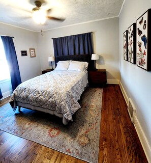 A bedroom with a bed, nightstands, a ceiling fan, a rug, and framed artwork on the wall. - 2-bed house, across the street from UNMC. (Omaha)