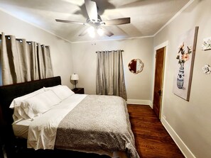 Een slaapkamer met een bed, een plafondventilator, een nachtkastje met een lamp, een deur en een muur met een lijst erin.
