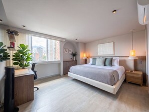 Une chambre moderne avec un grand lit, des tables de chevet, un bureau et une fenêtre donnant sur la ville.