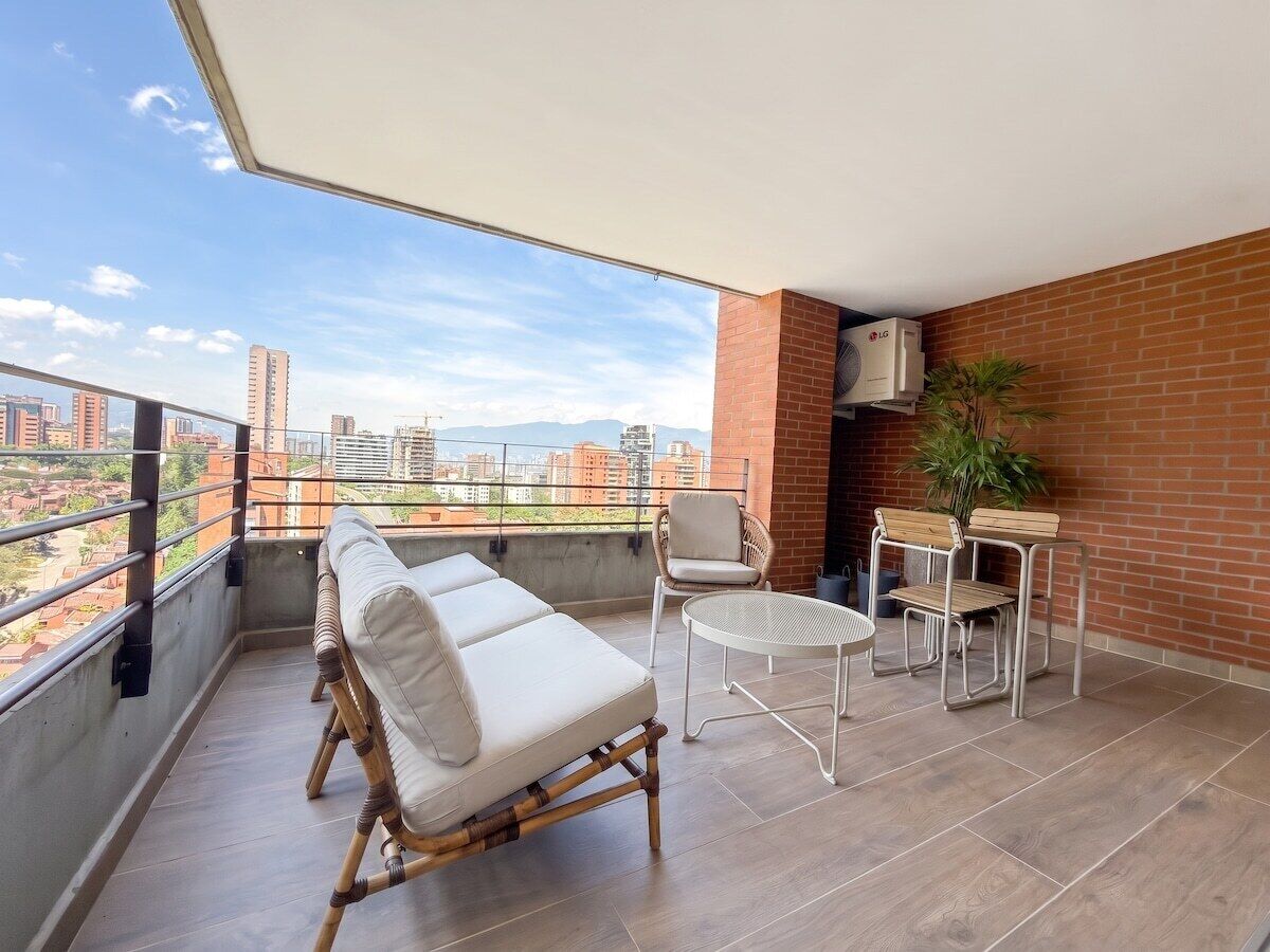 A balcony with a sofa, chairs, a table, and a potted plant.