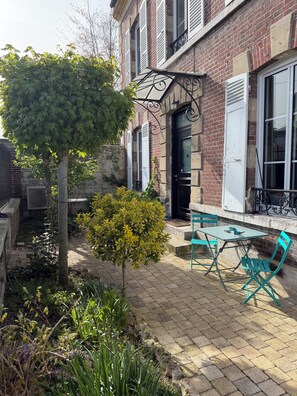 Une cour avec un bâtiment en briques, un petit arbre et une table entourée de chaises.