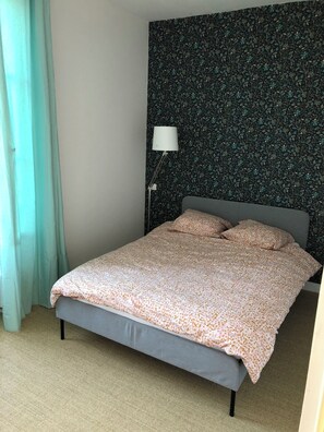 Un lit avec une couvre-lit à motifs, une lampe de chevet et un rideau.